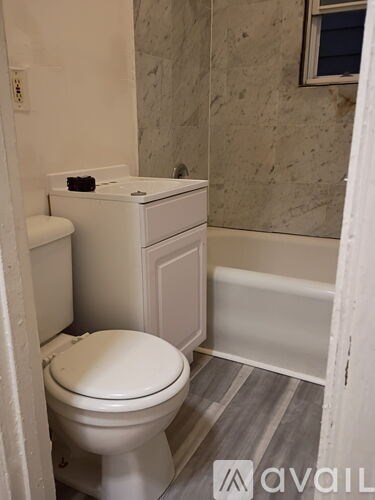 A white toilet with a white cabinet and a white bathtub in a bathroom.