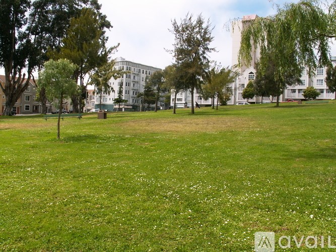 A grassy field with trees and buildings in the background.