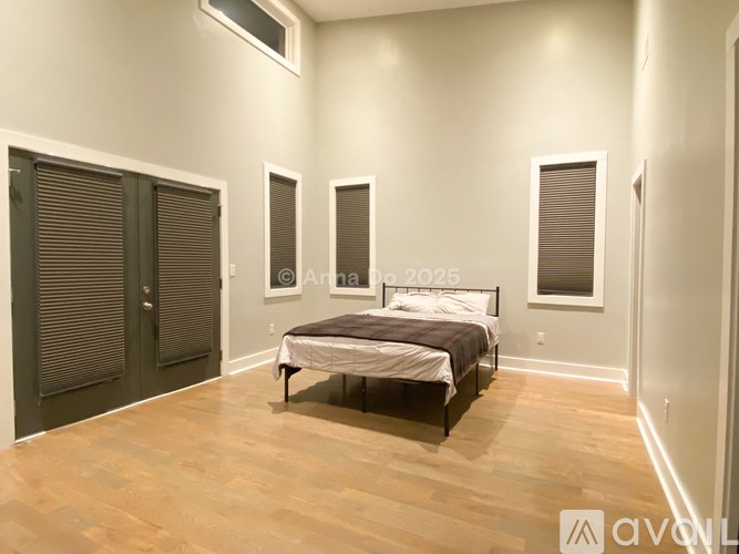 A bedroom with a bed, two windows, and a wooden floor.