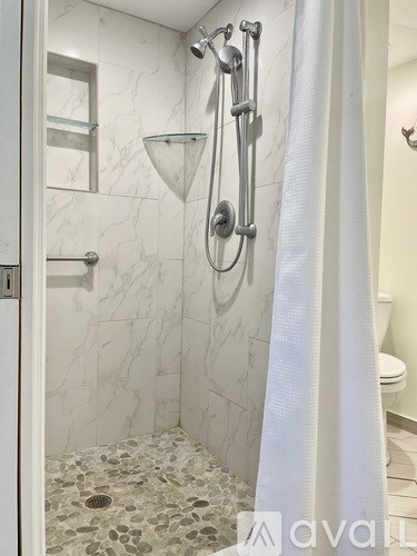 A white shower curtain hangs in front of a shower with a glass door.