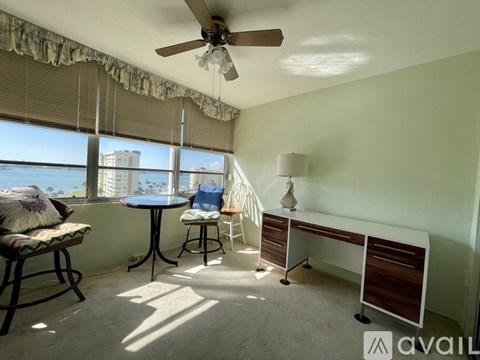 A room with a ceiling fan, a table with chairs, and a window with a view of the city.