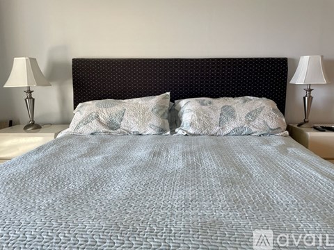 A bed with a grey comforter and two matching pillows sits between two lamps.