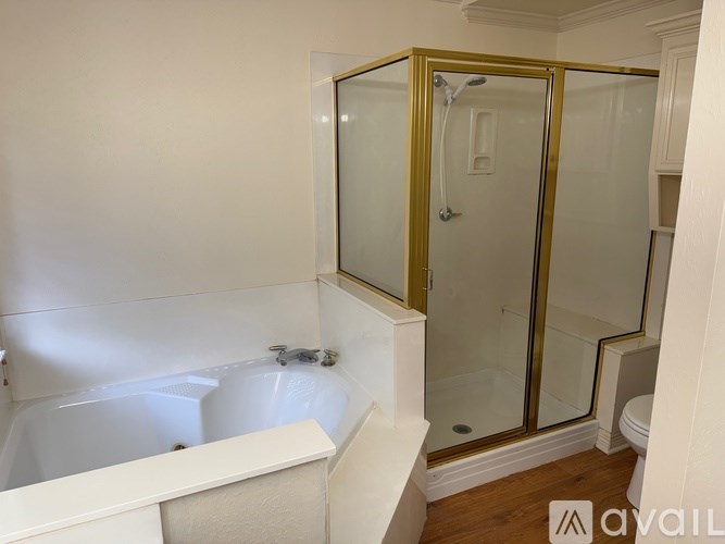 A bathroom with a white tub and a gold shower stall.