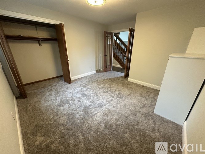 A room with a carpeted floor and a staircase in the background.