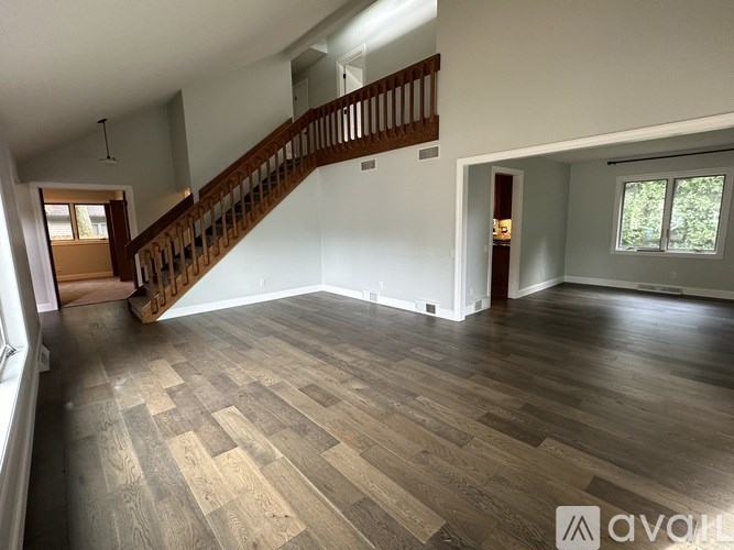 A spacious room with wooden flooring and a staircase.