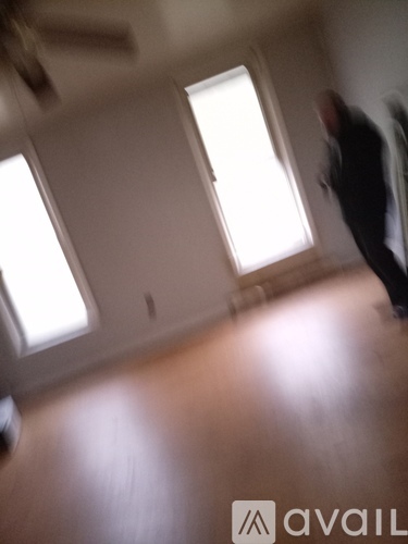 A man in a suit is walking through a room with wooden floors and two windows.