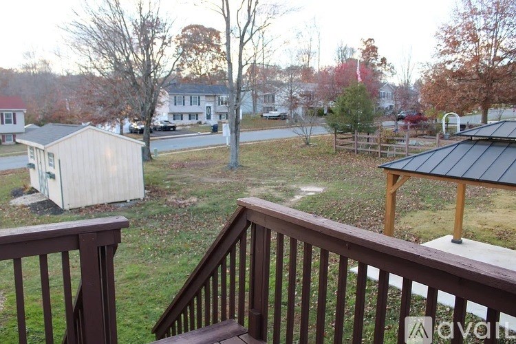 A deck overlooks a backyard with a shed, a tree, and a house in the background.