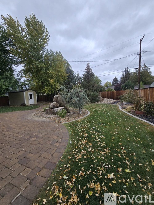 A backyard with a brick path and a grassy area with fallen leaves.