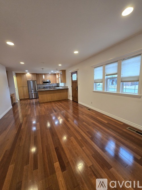 A room with wooden flooring and a kitchen area in the background.