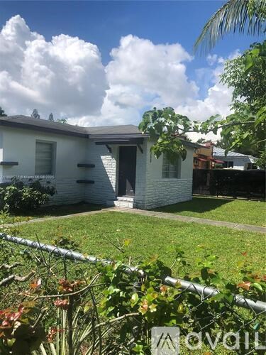 A house with a white exterior and a grey roof is surrounded by greenery.