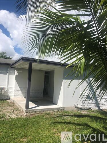 A white house with a porch and a palm tree in front.