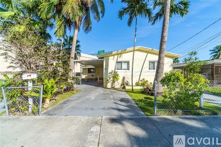 A house with a driveway surrounded by greenery and a fence.