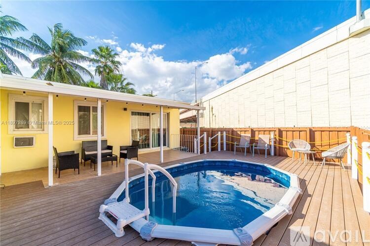 A pool on a wooden deck outside a yellow house.