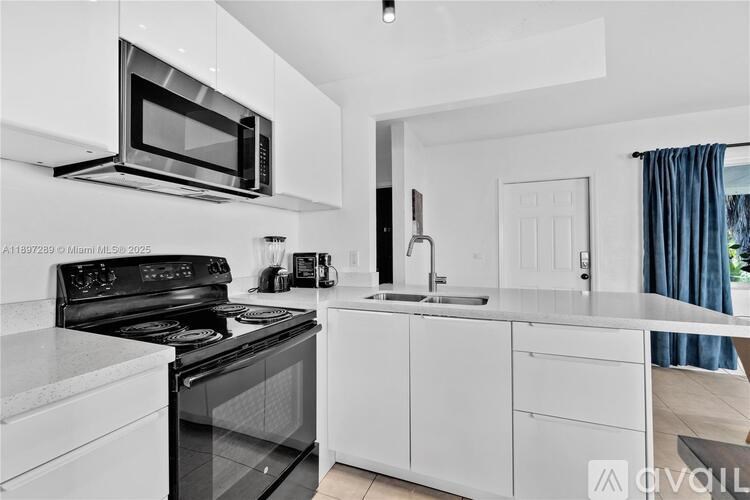 A modern kitchen with white cabinets and black appliances.