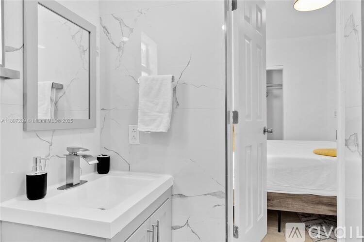 A white bathroom with a marble sink and mirror.
