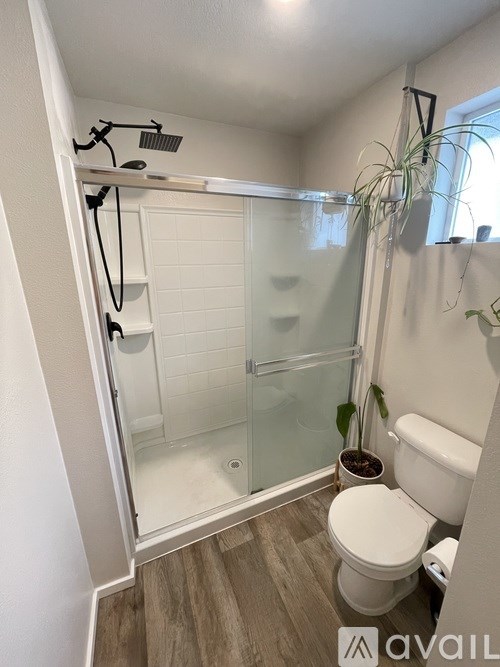 A small bathroom with a toilet, a glass shower stall, and a plant.