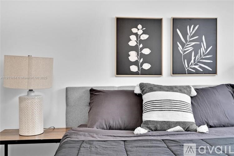 A bedroom with a grey bed, two pillows and two framed artworks on the wall.