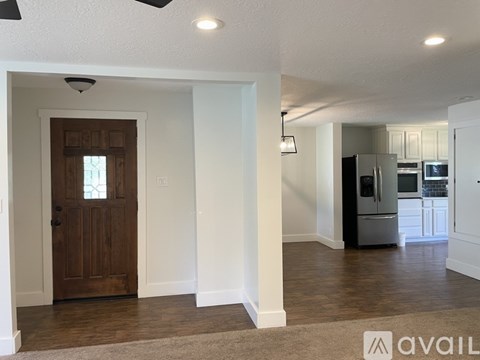 A spacious kitchen with white cabinets and a refrigerator is visible through a glass door.