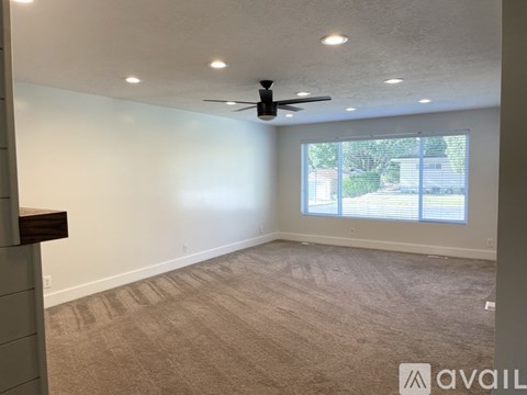 A room with a carpeted floor, a ceiling fan, and a window with blinds.