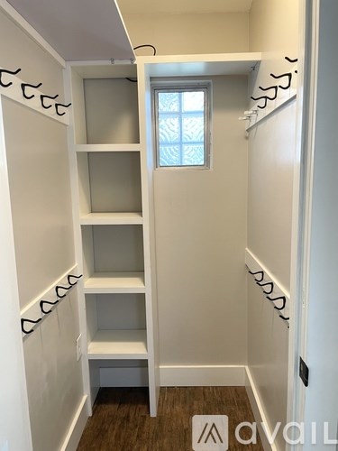 A white pantry with a window and a wooden floor.