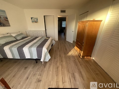 A bedroom with a bed, wooden floor, and a cabinet.