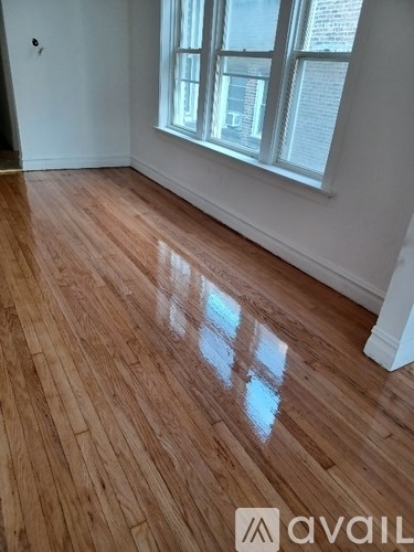 A room with wooden flooring and a window letting in sunlight.