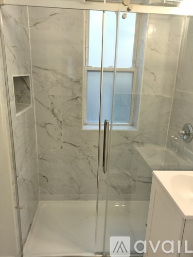 A bathroom with a marble wall and a glass shower door.