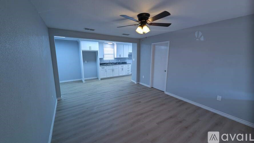 A room with a ceiling fan and a kitchen area in the background.