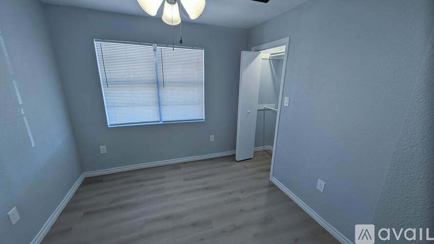A room with a window covered by blinds and a door on the right side.