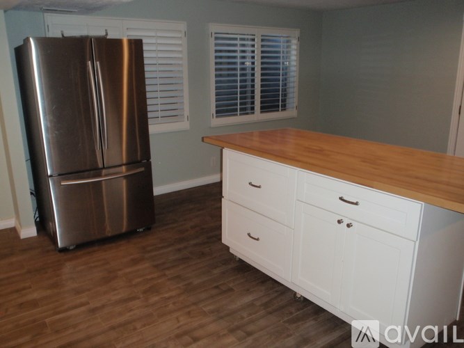 A kitchen with a stainless steel refrigerator, white cabinets, and a wooden countertop.