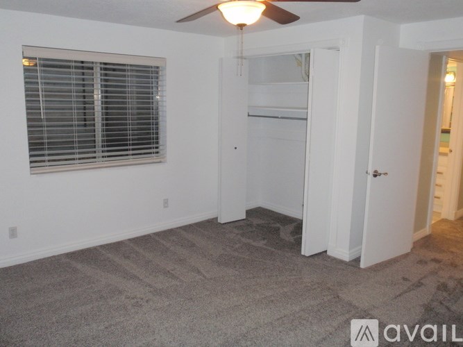 A room with a ceiling fan, a window with blinds, and a door leading to another room.