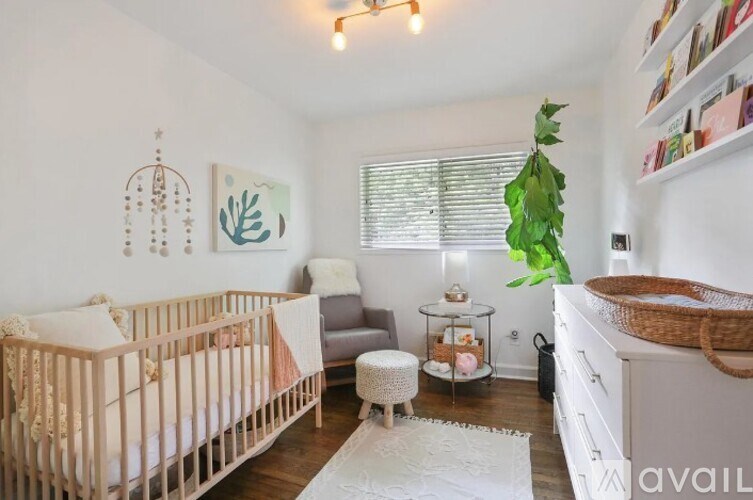 A baby's room with a crib, a chair, a plant, and a shelf with books.