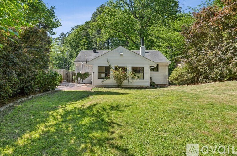A white house with a grey roof is surrounded by greenery.