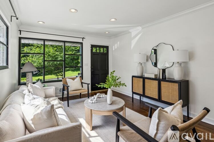 A living room with a white couch, a wooden coffee table, and a large window with a view of greenery outside.
