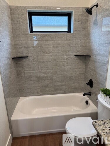 A bathroom with a white tub, toilet, and a window.