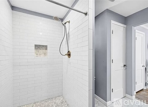 A white tiled bathroom with a shower head and a shower hose.