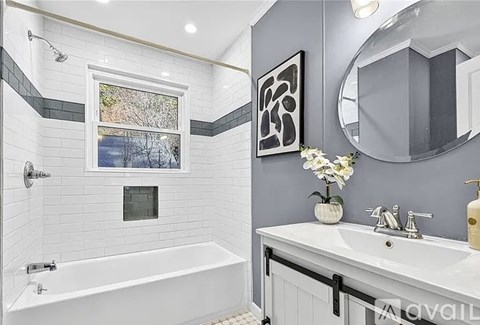 A bathroom with a white tub, sink, and a window with a view of trees.