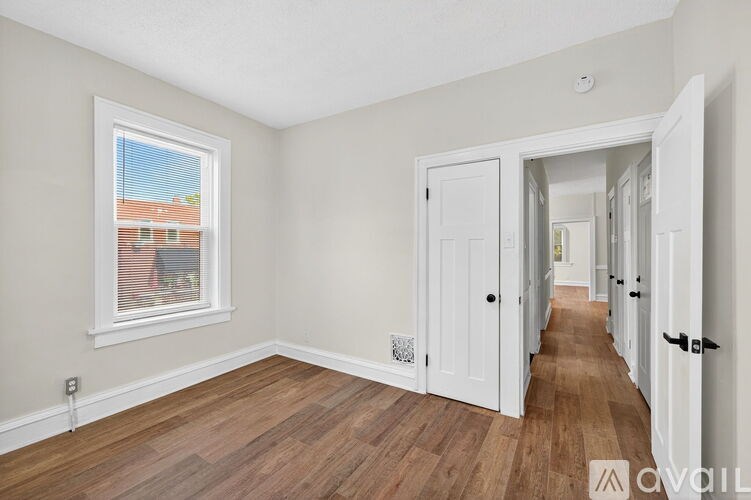 A room with wooden floors and white walls, leading to another room.