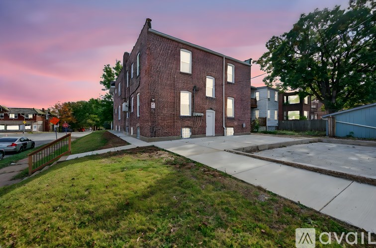 A brick building with a white door and windows is surrounded by a grassy area and a sidewalk.