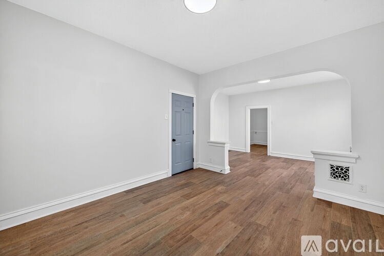 A spacious room with wooden flooring and white walls.