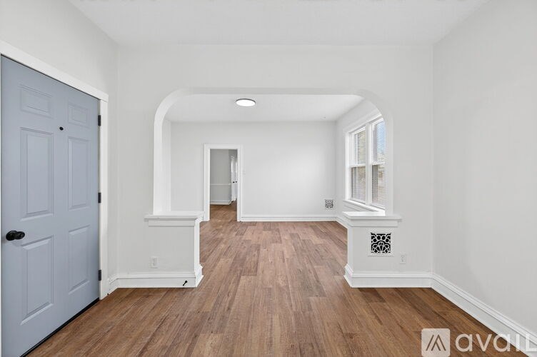 A room with a wooden floor and white walls, with a door on the left and a window on the right.