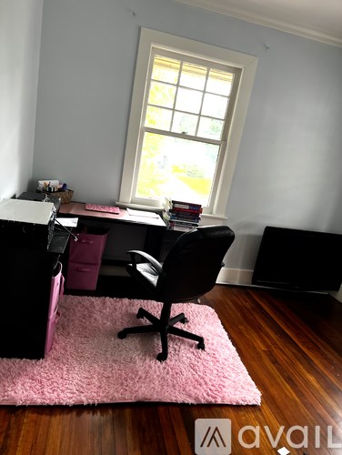 A black chair is in front of a desk with a pink rug on the floor.