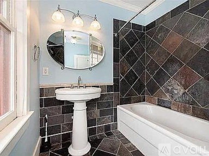 A bathroom with a white pedestal sink, a bathtub, and a mirror.