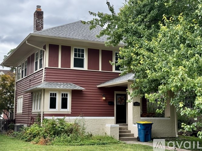 A red house with a blue trash can in front.