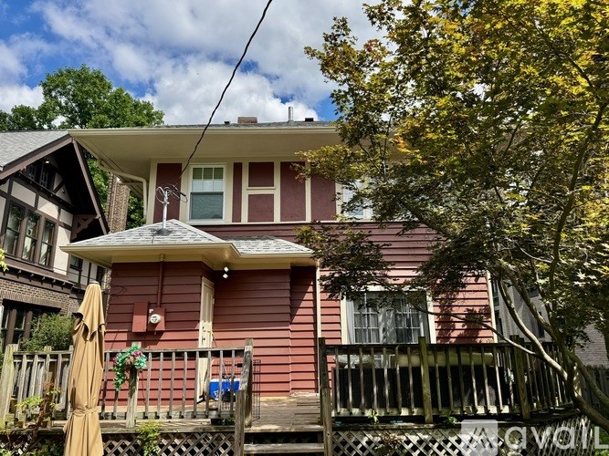 A red house with a porch and a tree in front.