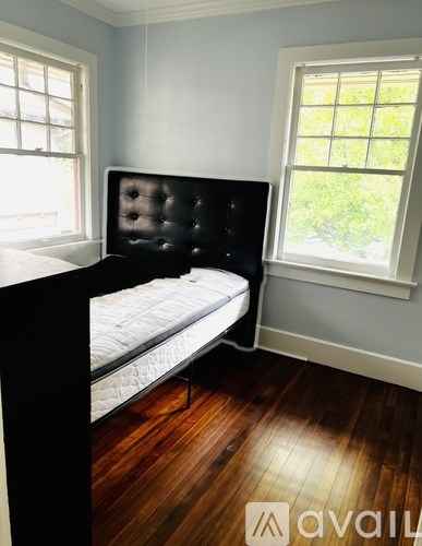 A black tufted headboard bed with a white mattress in a room with wood flooring.