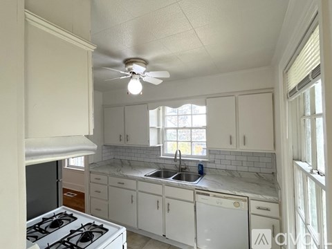 A white kitchen with a stove top oven and a fan on the ceiling.