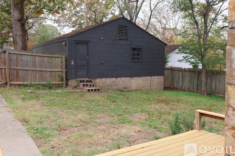 A black shed sits in a backyard with a wooden fence and a wooden deck.