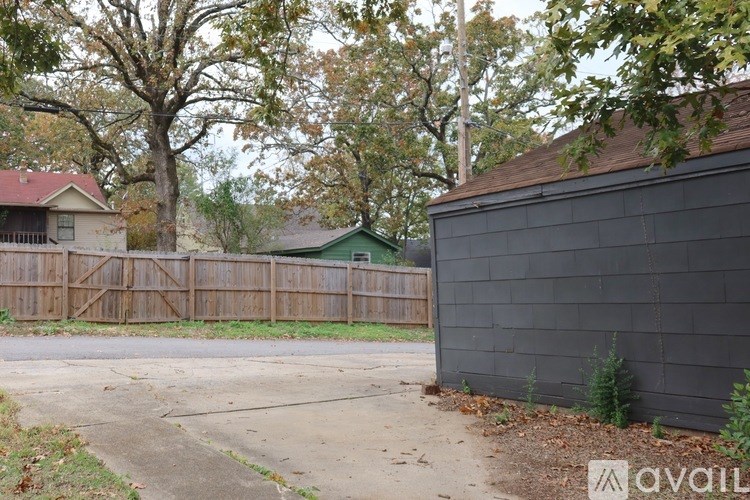 A black house with a brown fence and a tree in front.