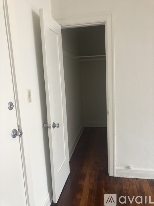 A white door with a silver handle is open to a dark hallway.